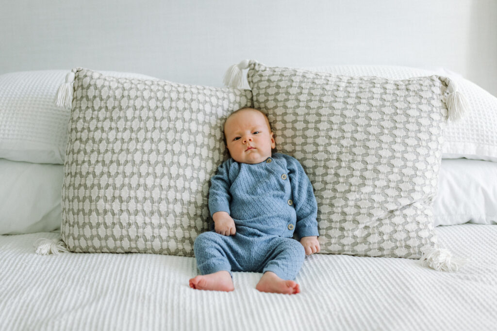 alert newborn sitting up against bed pillows in-home newborn session Alameda
