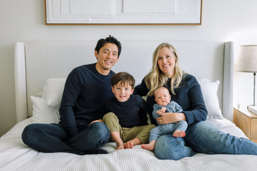 family of four sitting on bed during in-home newborn session Alameda
