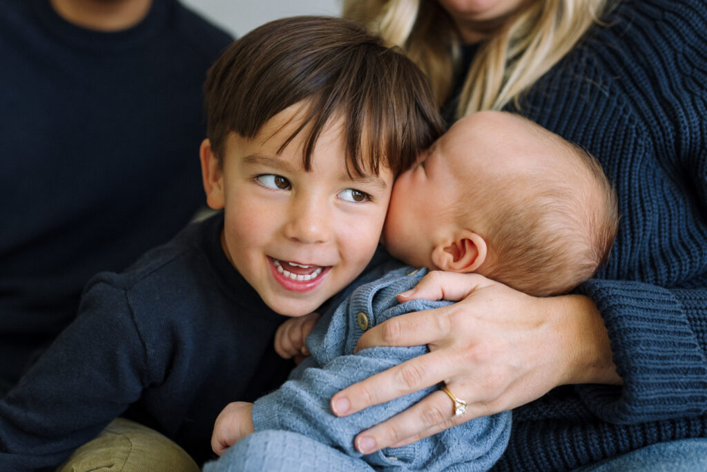 toddler pressing face against newborn sibling as if being kissed in-home newborn session East Bay