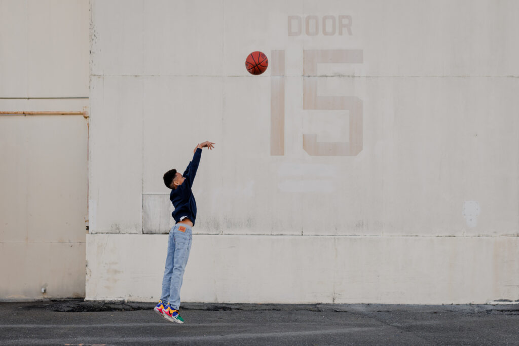 boy throwing basketball up like he is shooting a basket at Alameda Naval base hangar