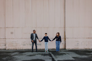 Family holding hands in front of a large industrial hangar wall during an Alameda family photography session