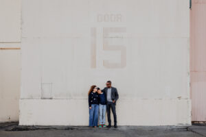 Family of three in a wide shot against a large industrial hangar wall during an East Bay family photography session
