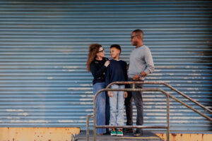mom, dad, and son standing in front of blue garage door at Alameda Naval Base looking at each other