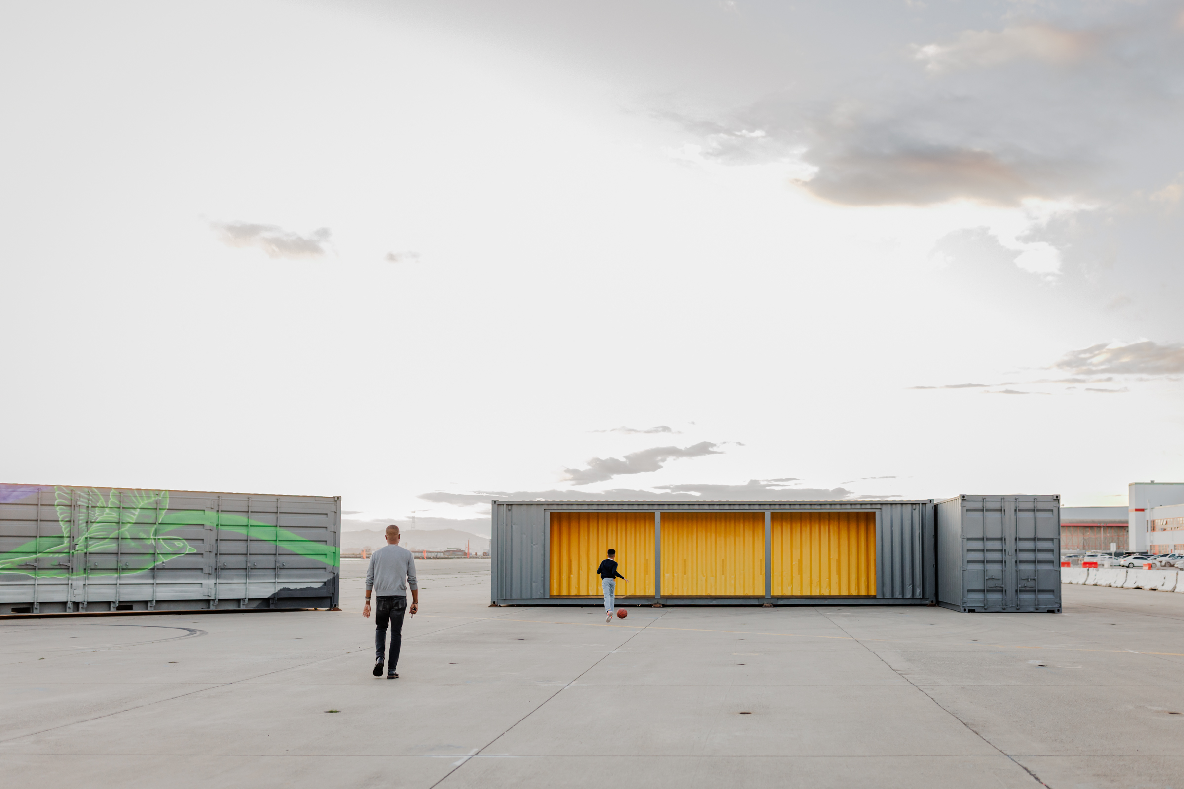 Dad and son walking toward a yellow shipping container on an open tarmac during a family photography session