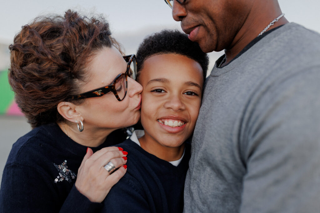 Mom kissing her son on the cheek while dad hugs them both during a family photography session at the Alameda Naval Base