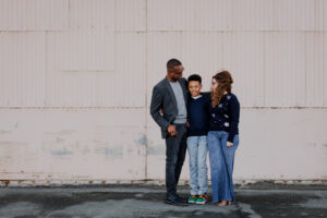 Family of three standing together against a large industrial hangar wall during an East Bay family photography session
