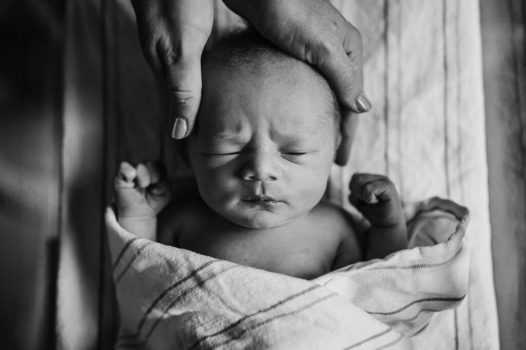newborn laying in hospital bassinet with mom's hands cradling his head