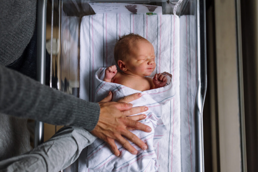 newborn laying in bassinet with parents hands resting on him Fresh 48 session