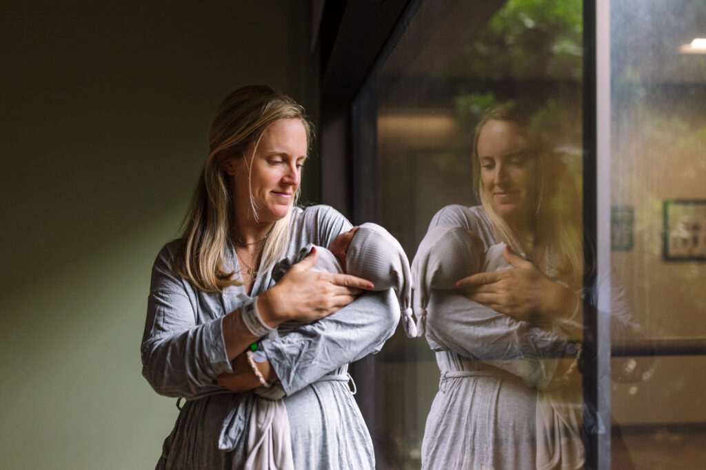 mom holding newborn by hospital window during Fresh 48 session Berkeley