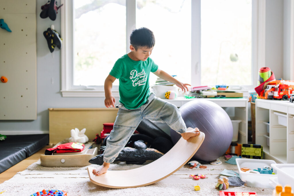 Boy balancing on a wooden rocker board in his bedroom during an in-home family session in the East Bay