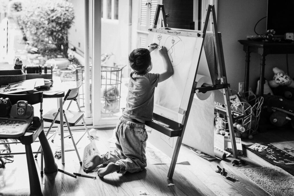 Boy drawing on an easel in natural window light during an in-home family session in the Bay Area