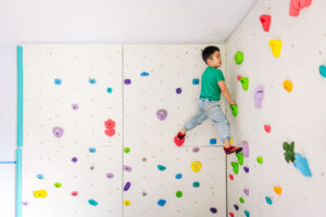 boy at the top of a colorful climbing wall during in-home family session in Bay Area
