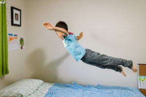 Boy jumping off his bed with arms outstretched during an in-home family photography session in the East Bay