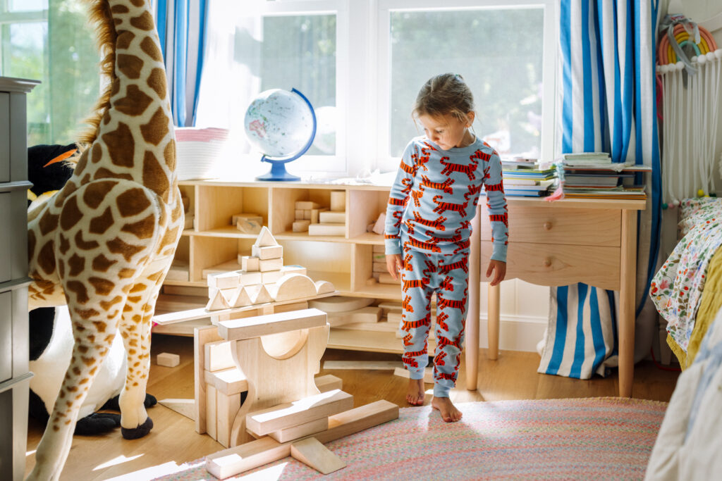 Young girl in tiger pajamas standing next to a block structure in her bedroom during an in-home family session in the East Bay