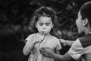 Young girl blowing a dandelion while her brother reaches in during an outdoor family session in the Bay Area