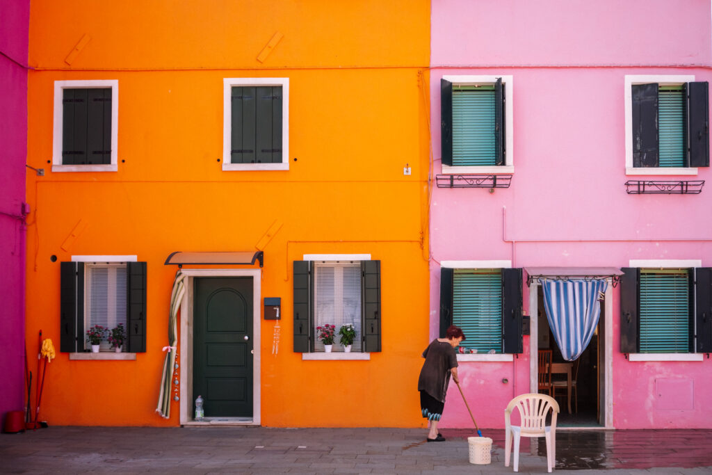 Woman sweeping porch in front of colorful buildings in Burano, Italy