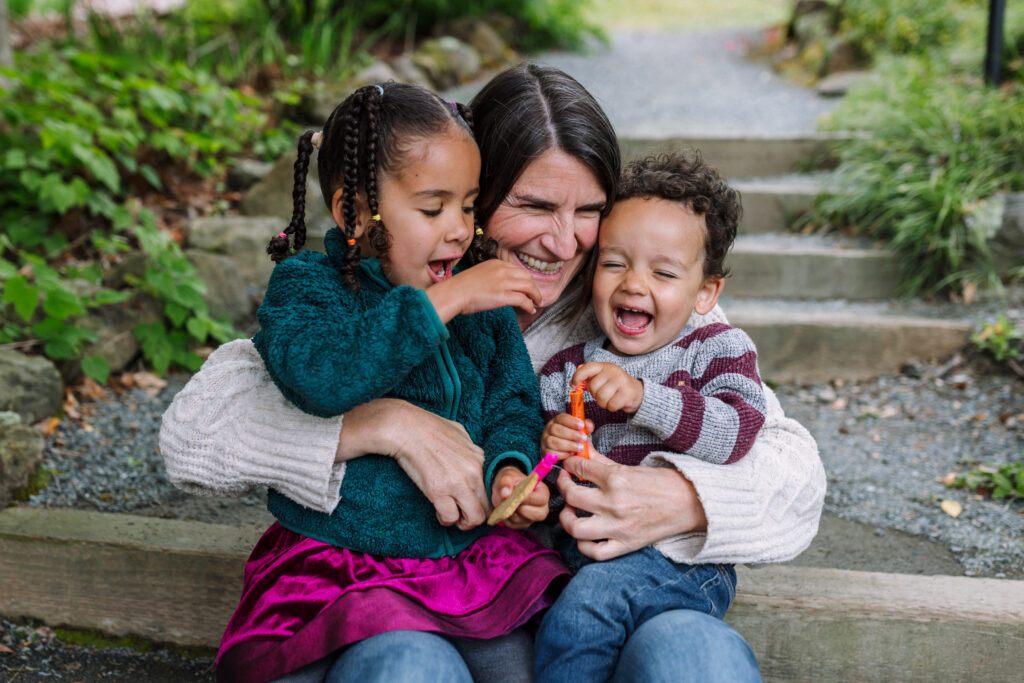 A mother sits on garden steps at the UC Botanical Garden in Berkeley, holding both young children as all three laugh together