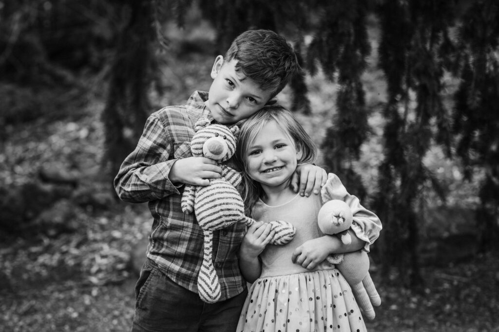 A brother and sister stand together holding their stuffed animals at the UC Botanical Garden in Berkeley