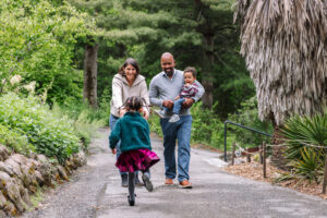 A young girl runs toward her parents along a garden path at the UC Botanical Garden in Berkeley, her father holding their baby son as her mother reaches out to her