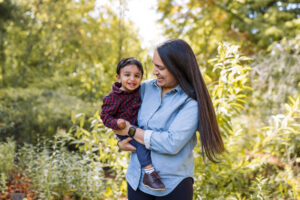 A mother holds her toddler son in the garden at the UC Botanical Garden in Berkeley, both smiling in warm afternoon light