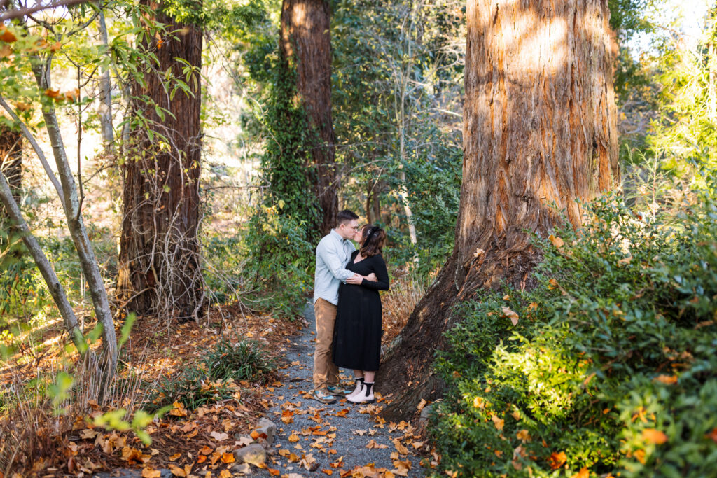 A couple shares a quiet moment on a garden path lined with fall foliage and redwood trees at the UC Botanical Garden in Berkeley